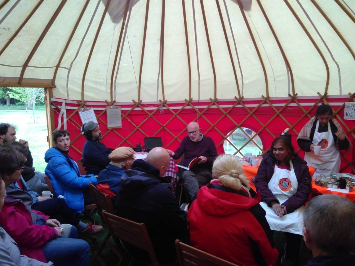 People sitting inside a yurt listening to another person talk.
