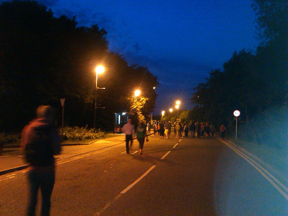 A crowd of people walking down a street lit by streetlights.