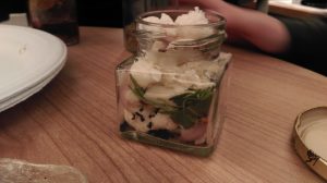 Small glass jar filled with foraged white petals and green leaves
