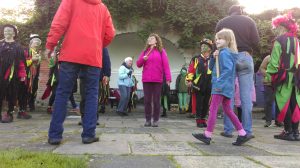 A group of adults and children assembled outside with morris dancers for a workshop
