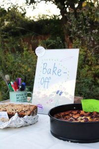 Various baked goods displayed on a table outdoors with a sign saying Bake Off