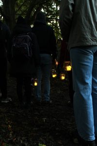 A group of people walking through the woods at twilight carrying night jar lights